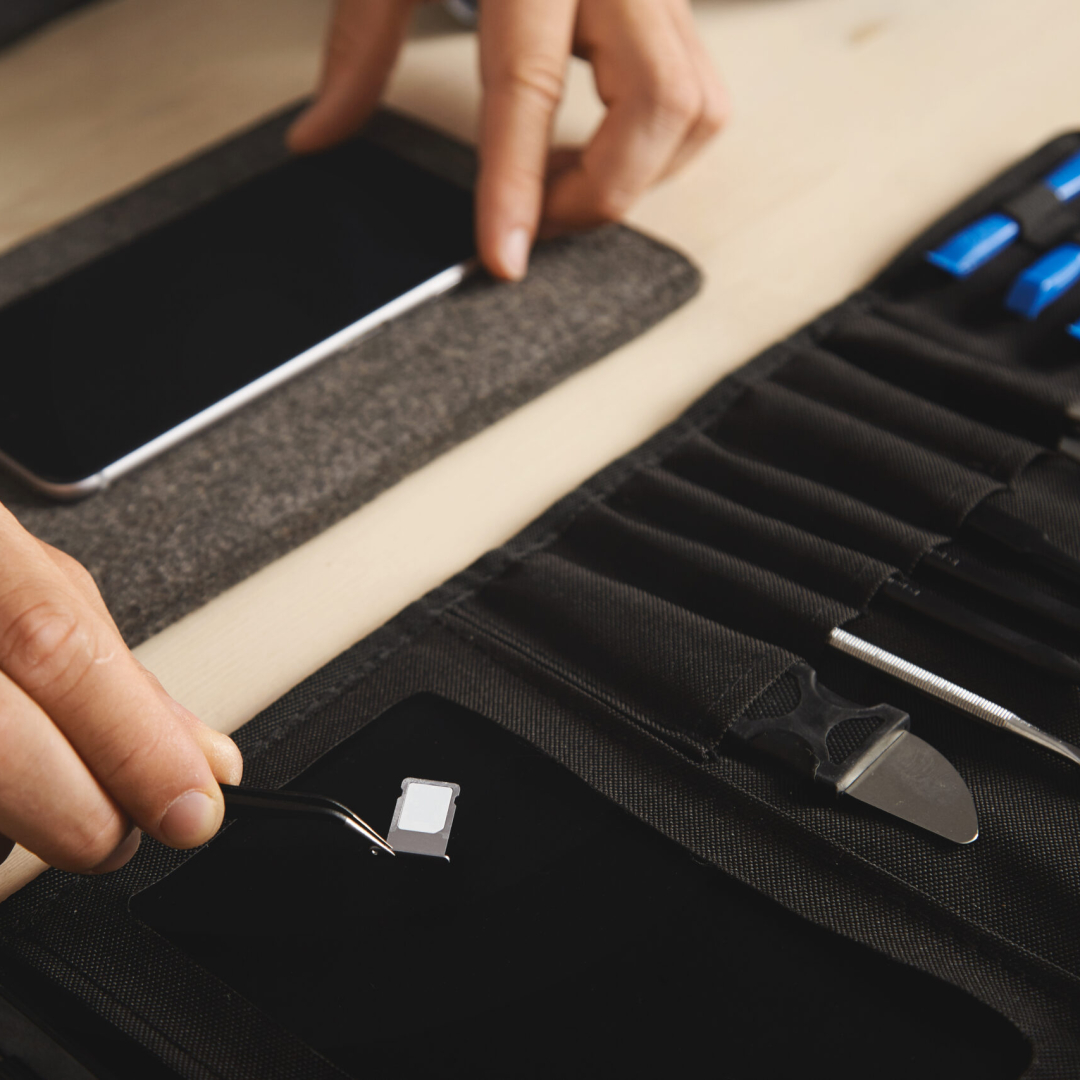 Close up on hand with pincher tool holding sim-card slot with nano sim above black magnet plate on portable tookit for electronic repeirment service